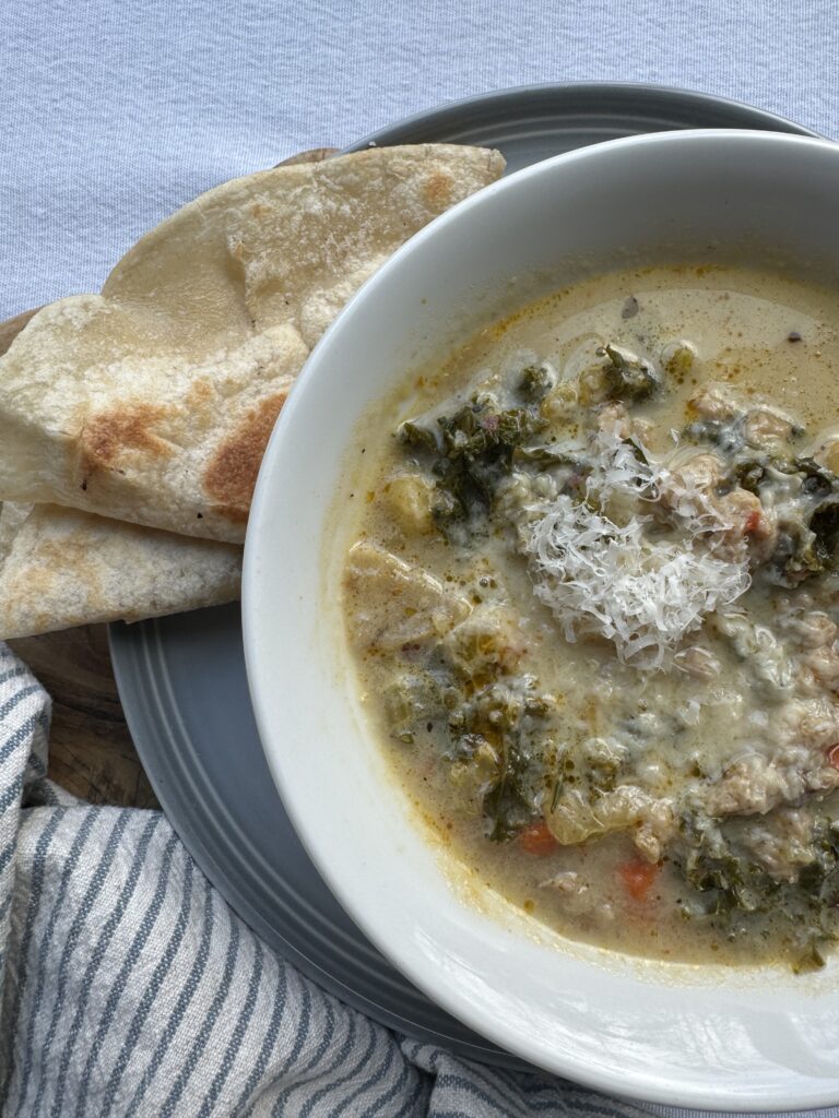 Finished soup served in a white bowl, a side of flatbread, with a striped napkin.