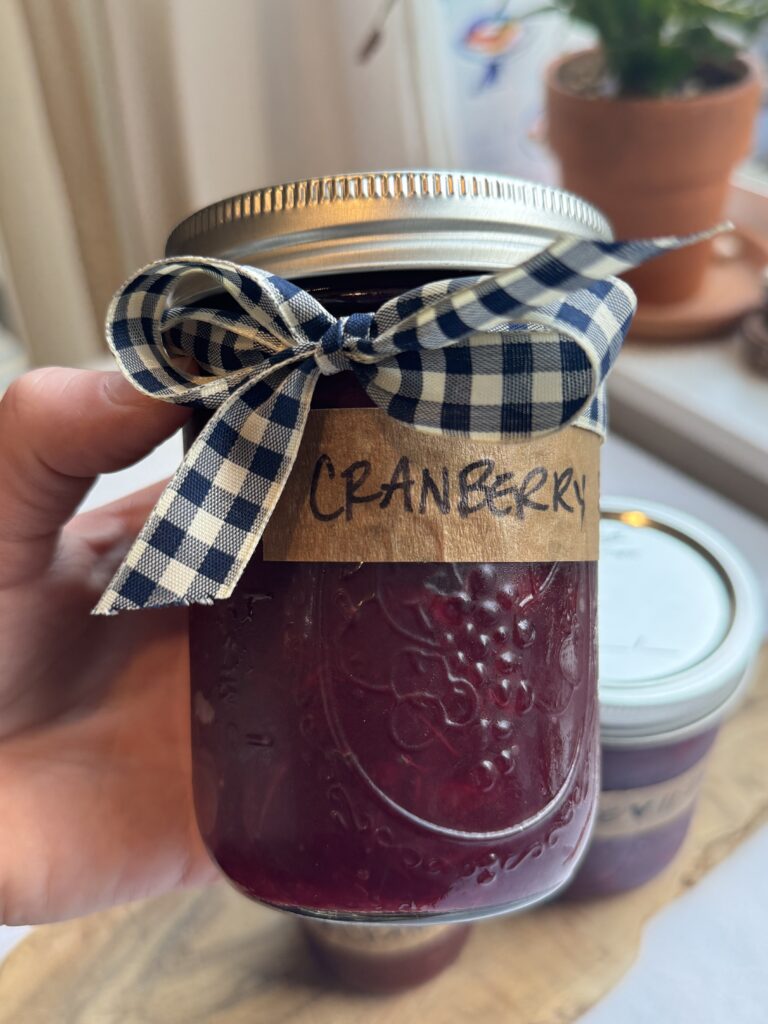 A jar of Whole Berry Cranberry Sauce labeled and finished with a blue and white checkered ribbon bow tied around the jar.