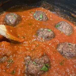 Meatballs stewing in a red marinara sauce.