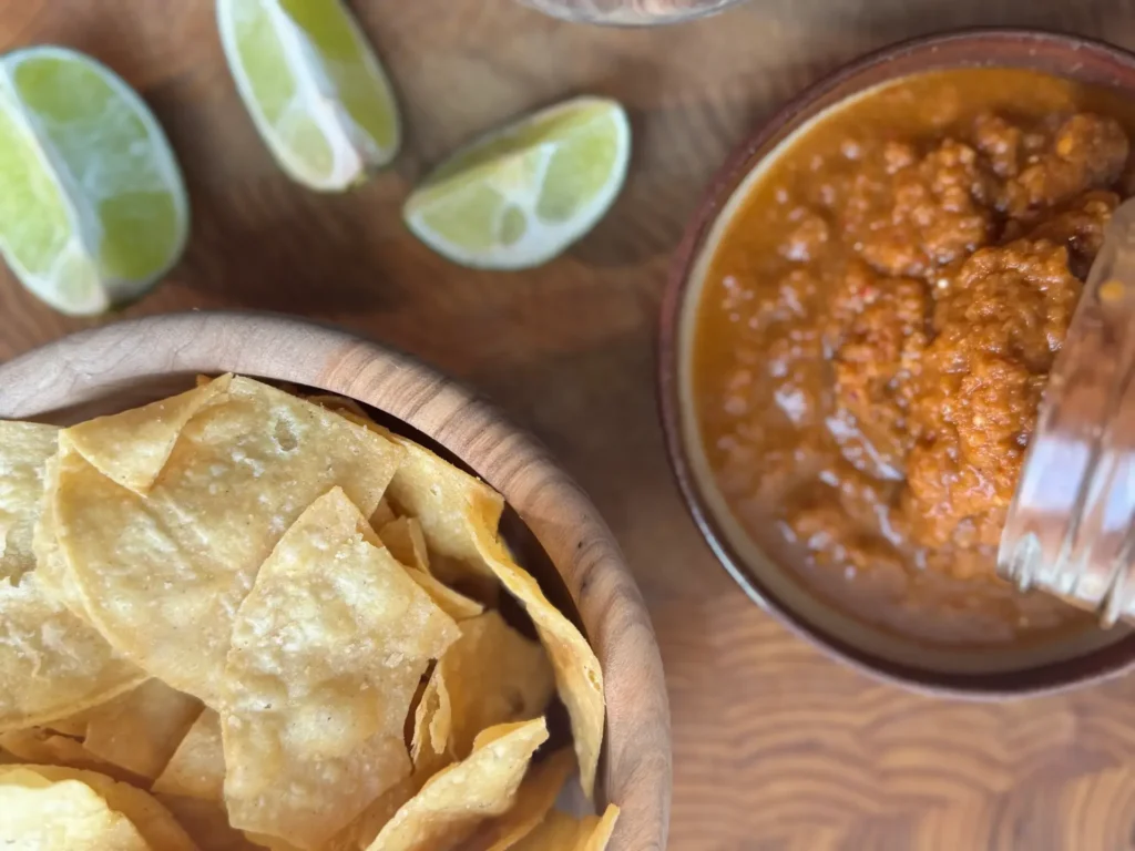 Overhead shot of restaurant-style tortilla chips, a bowl of Spicy Jalapeno Salsa, and some sliced limes on the side.