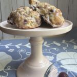 Finished scones on a small, light pink cake stand with a bowl of cherries to the right of the scones.