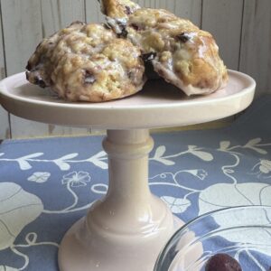 Finished scones on a small, light pink cake stand with a bowl of cherries to the right of the scones.