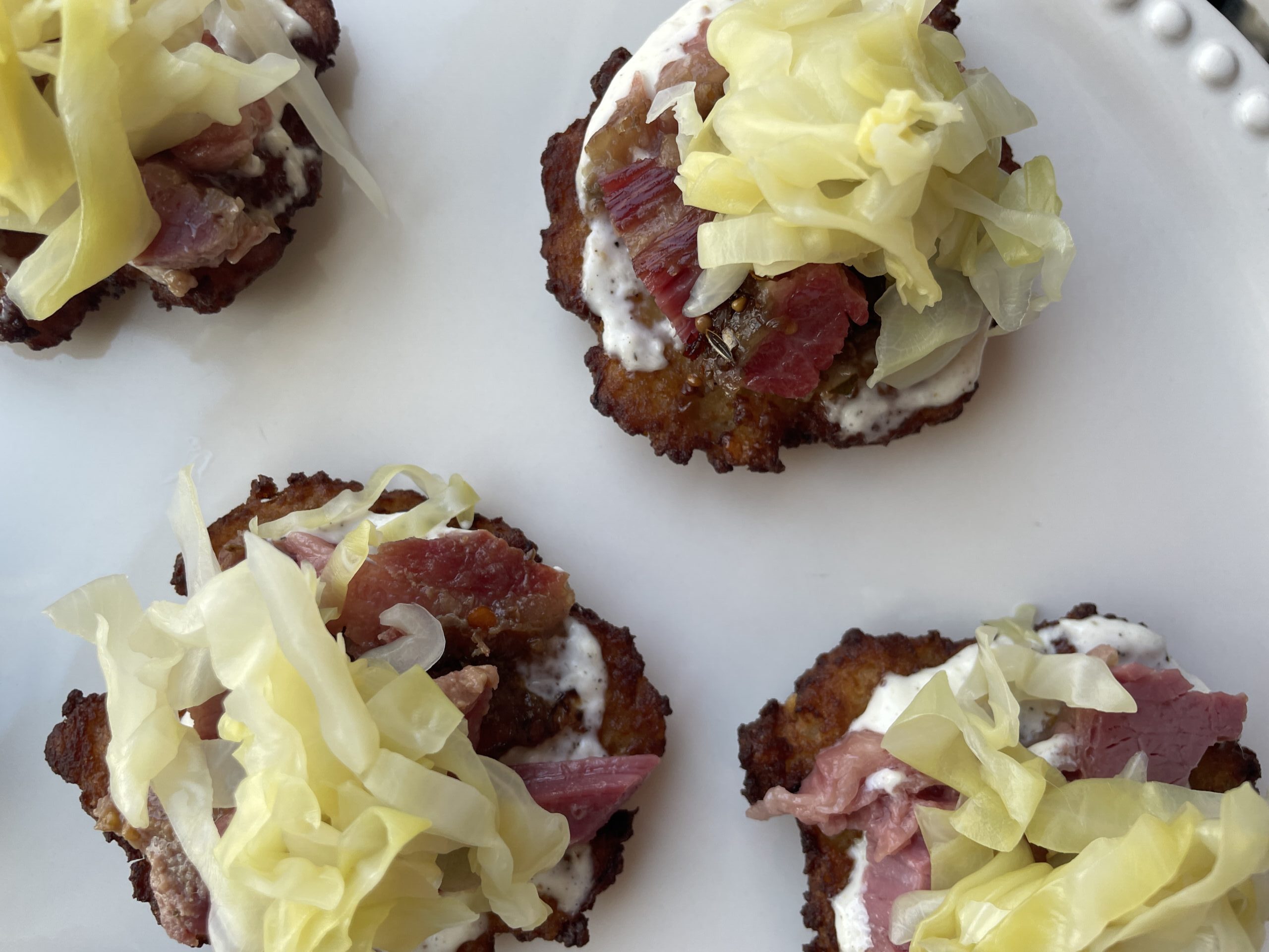 Overhead image of finished product: potato latkes with corned beef and cabbage, on white platter.