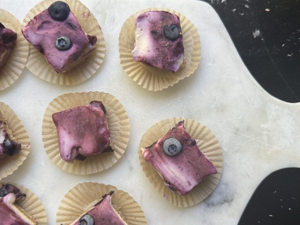 Overhead view of sliced No-Bake Blueberry Cheesecake Bars on a serving board in individual liners.