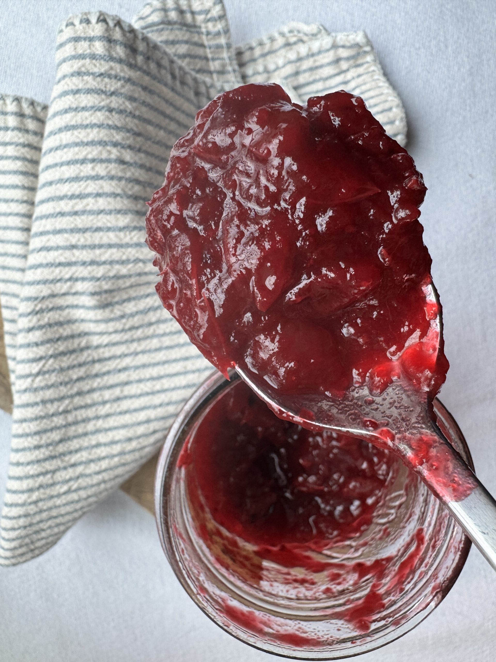 Finished cranberry sauce in a jar being spooned out. Striped napkin to the side.