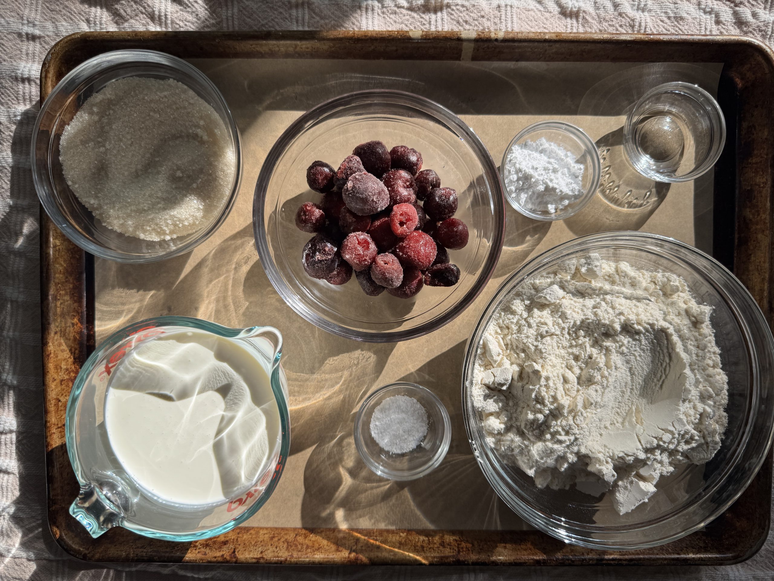 Overhead view of all ingredients for Cherry Almond Scones: All purpose flour, sugar, baking powder, salt, cream, almond extract, and black cherries.