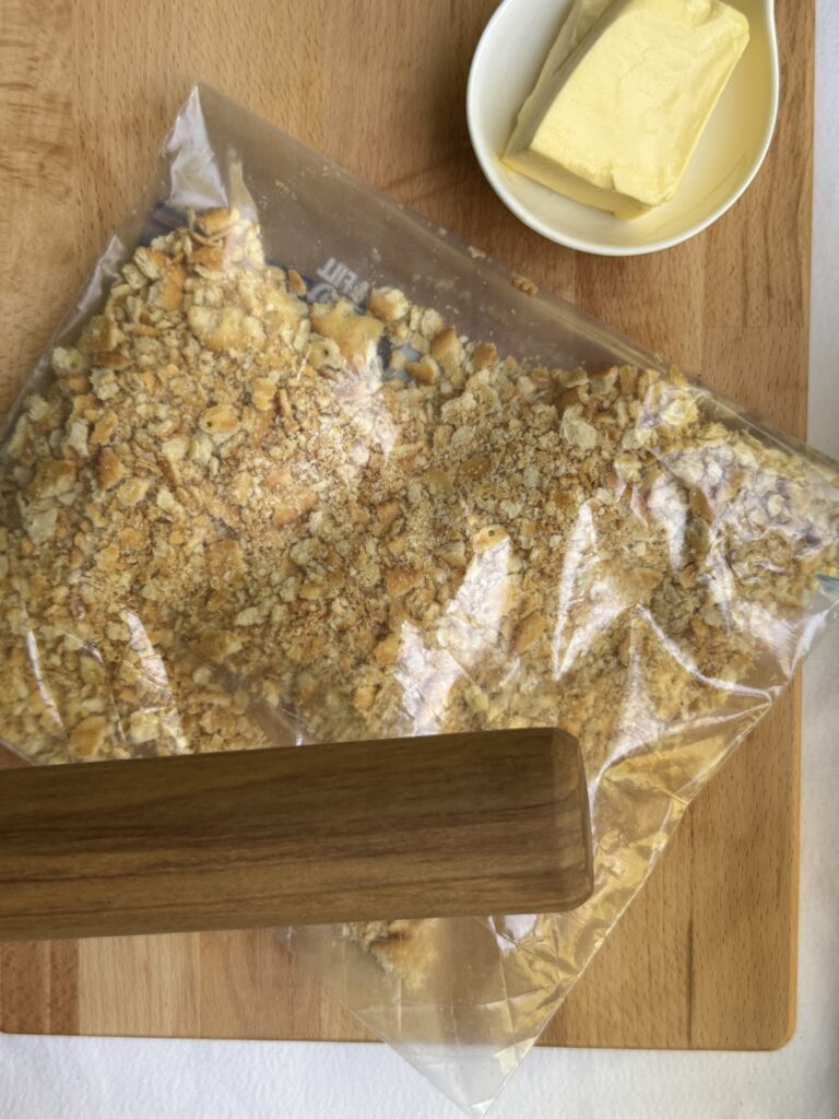 Broken up Ritz crackers in a zip top bag, next to a rolling pin.