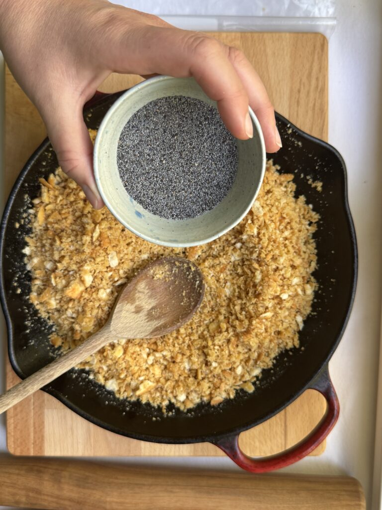 Poppyseeds being added to Ritz cracker crumble in a skillet.