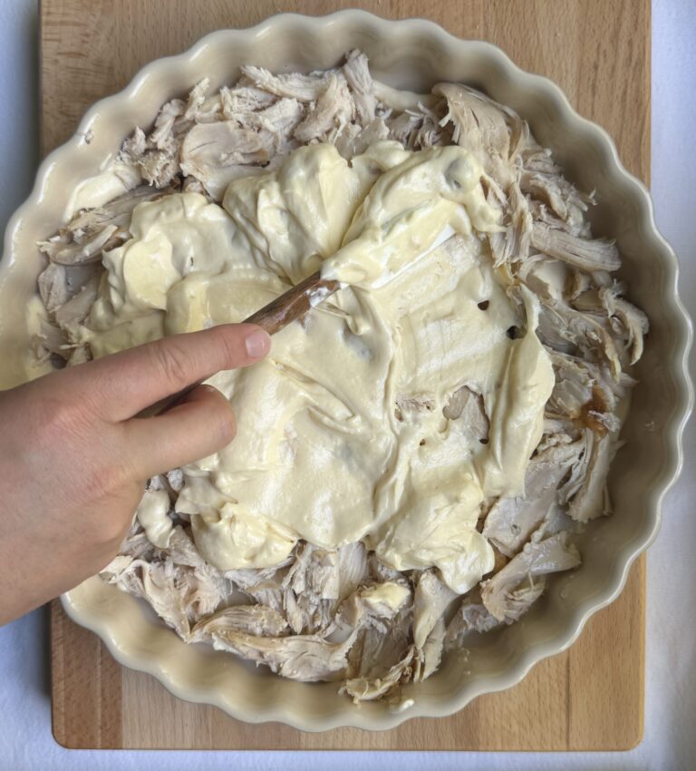 Chicken pieces in the base of the baking dish, creamy sauce being spread over top.