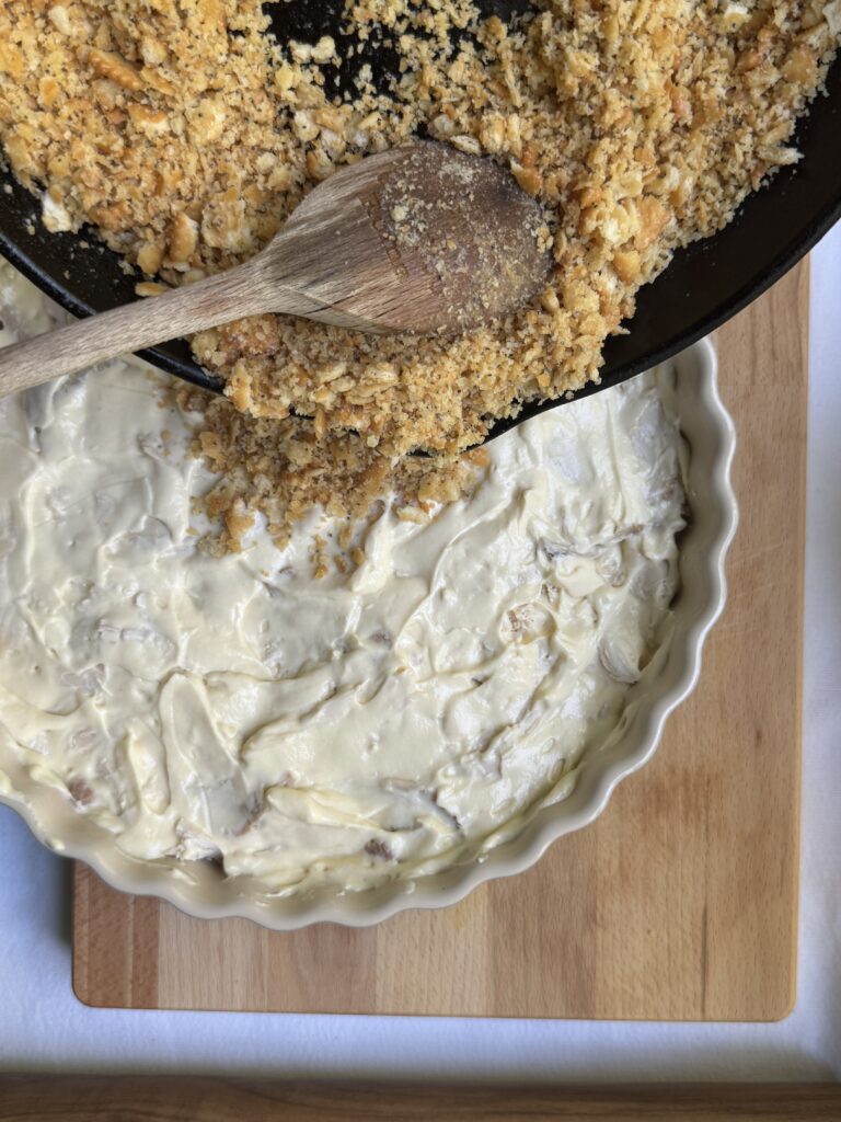 Ritz cracker crumble being spooned onto the top of the casserole.