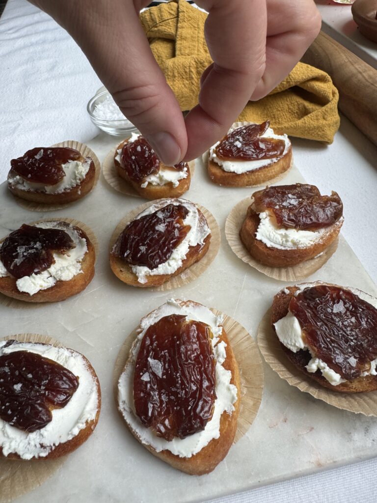 Crostini with goat cheese and dates, and a hand sprinkling flaky salt on top.