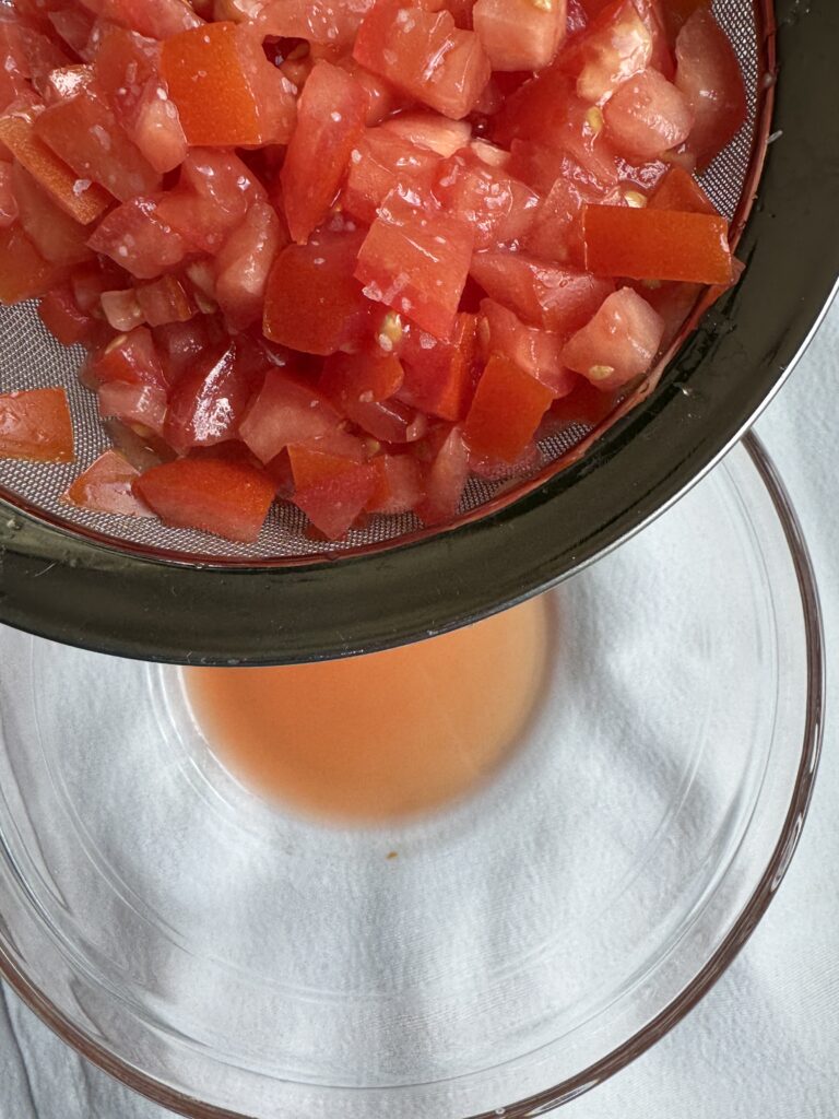 Diced tomatoes with a pinch of Kosher salt, sitting in a colander, straining the excess water.