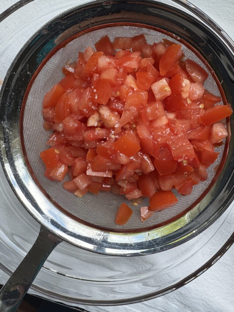 Diced tomatoes with a pinch of Kosher salt, sitting in a colander, straining the excess water.
