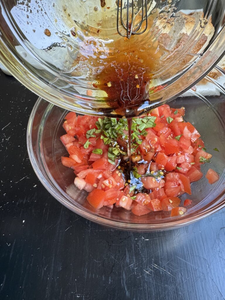 Balsamic-olive oil mixture being poured over top of the tomatoes and herbs.
