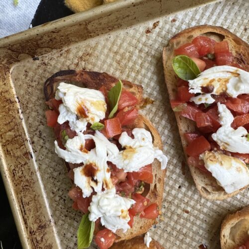 Burrata bruschetta toasts, topped with balsamic vinegar and basil leaves.