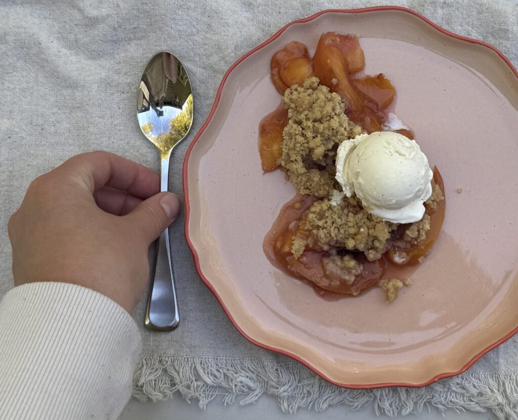 Nectarine Crumble on a peach-colored plate, topped with vanilla ice cream.