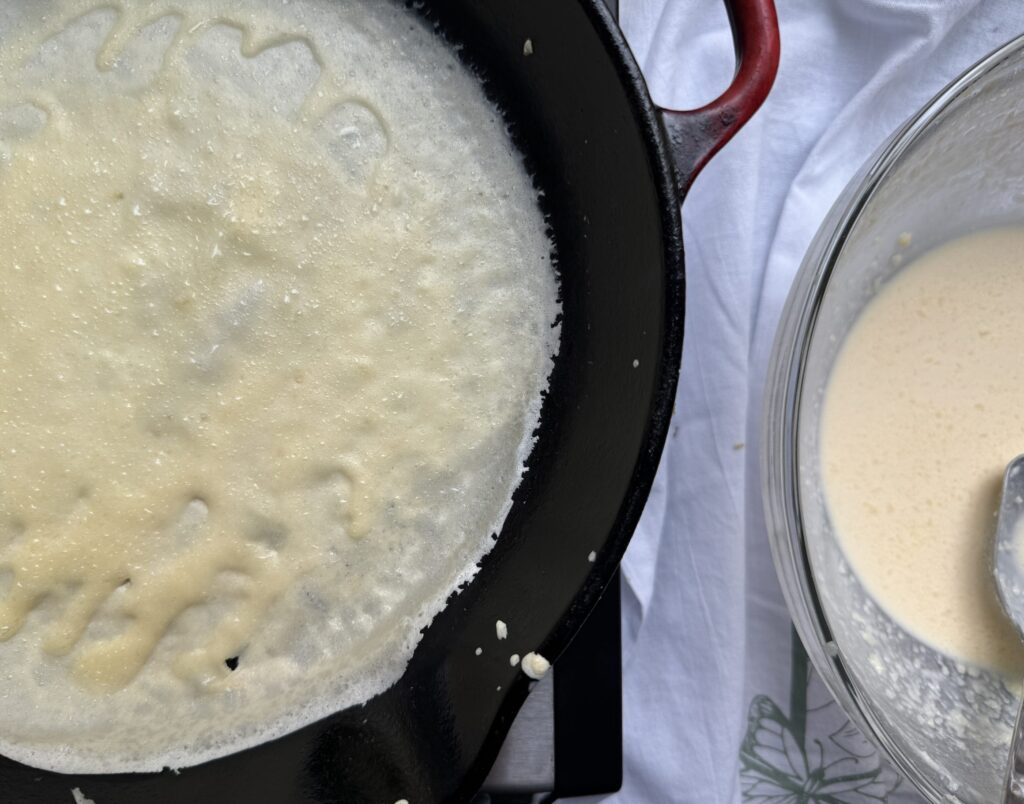 Crepe batter cooking in a cast iron skillet.