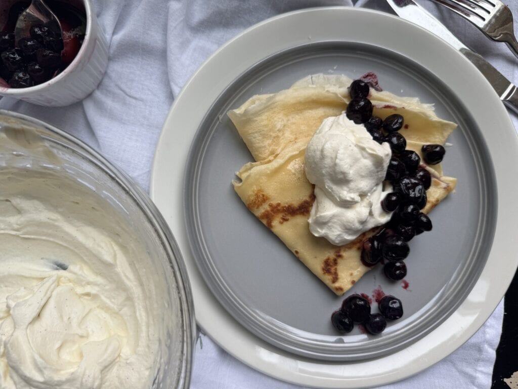 Plated crepes with blueberry compote and a bowl of vanilla bean whipped cream.