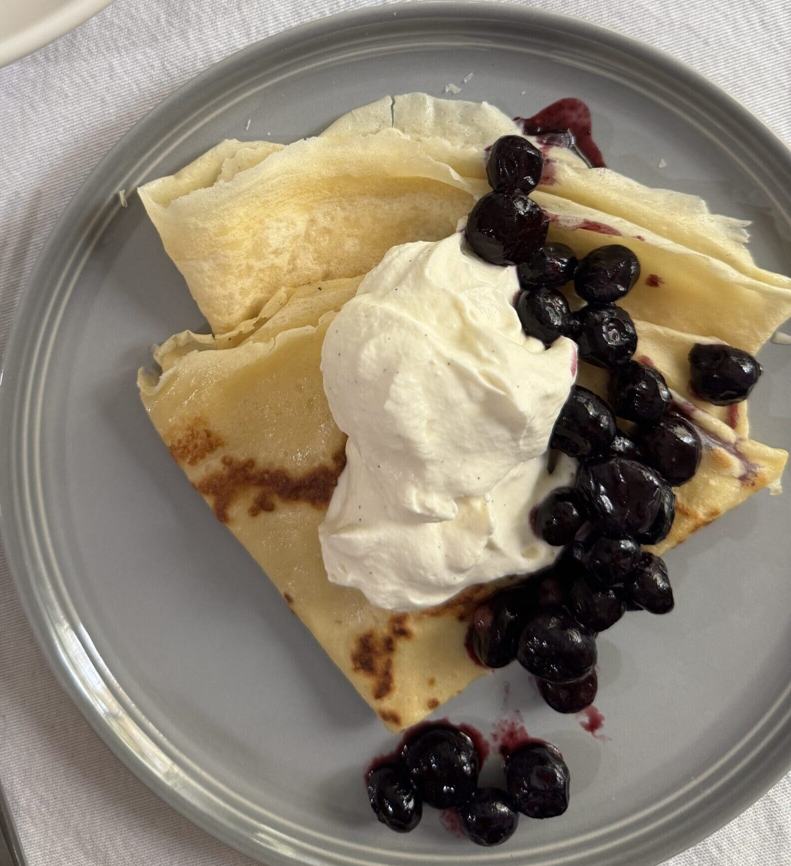 Two crepes, perfect for one person, served with vanilla bean whipped cream, blueberry compote, and a side of sausage.