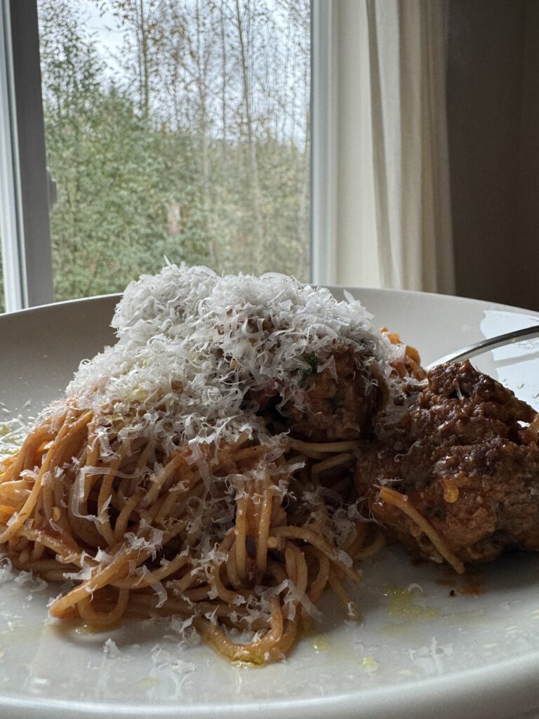 Finished Oven-Roasted Meatballs in red sauce with pasta and parmesan cheese.