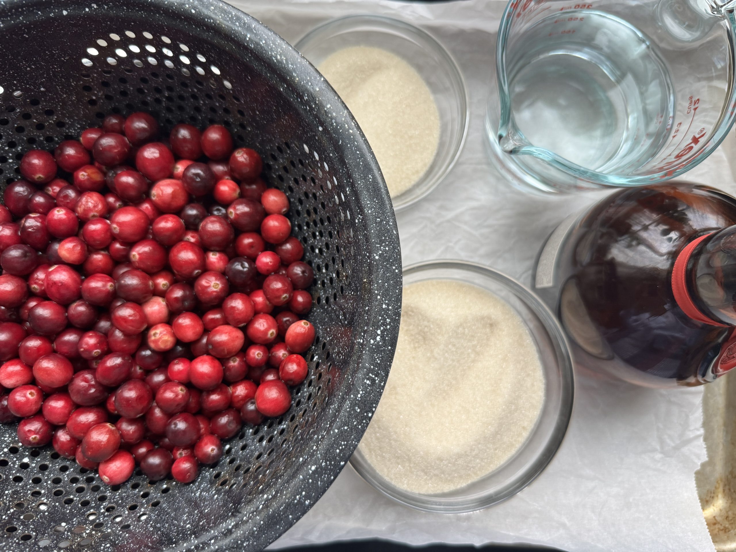 Ingredients for Sparkling Cranberries: cranberries in a colander, granulated sugar, water, and optional orange liqueur.
