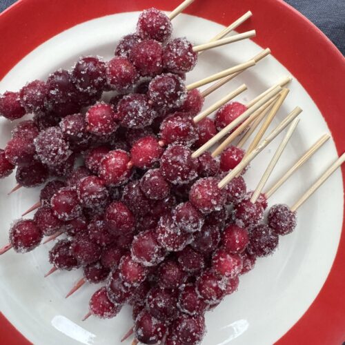 Sparkling Cranberries on wooden skewers, served on a white plate with red trim.