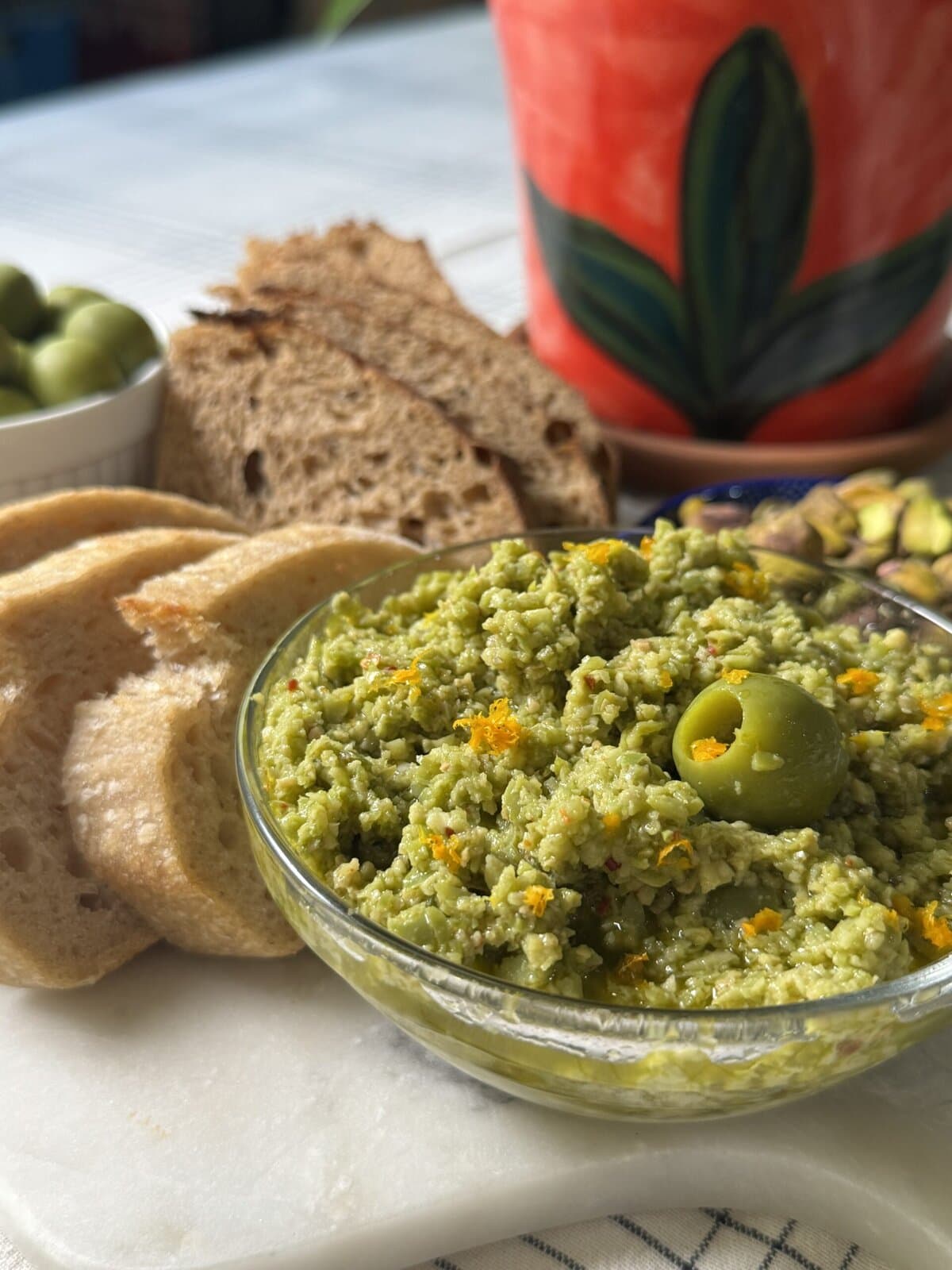 Olive tapenade with sliced bread and whole green olives.