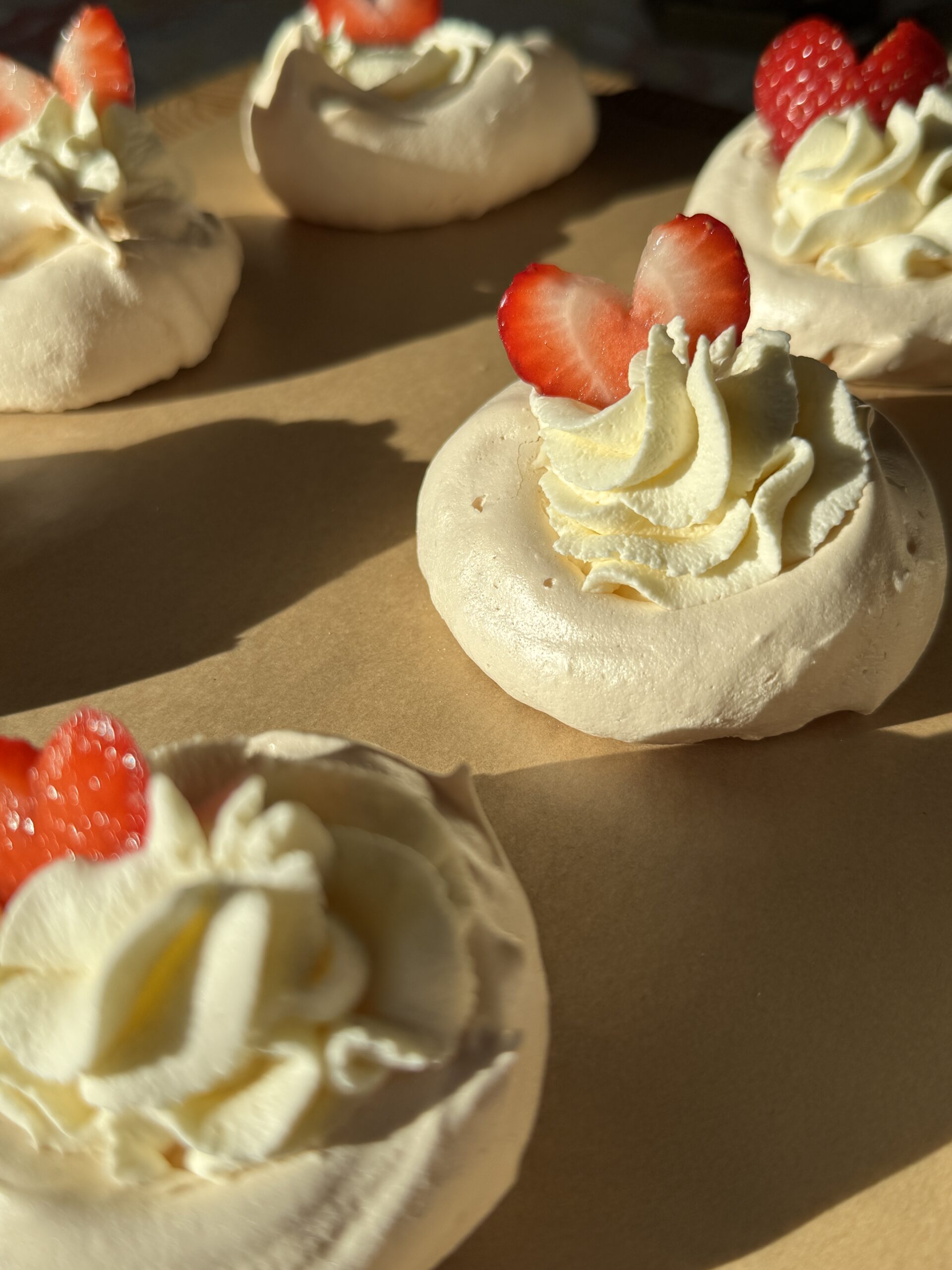 Mini pavlova nests topped with vanilla bean whipped cream and strawberry hearts.
