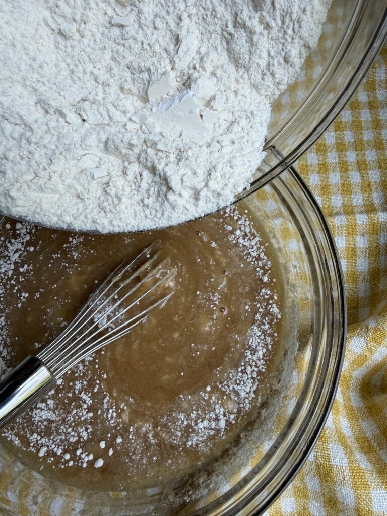 Dry ingredients pouring into wet ingredients for banana walnut bread with chocolate chips.