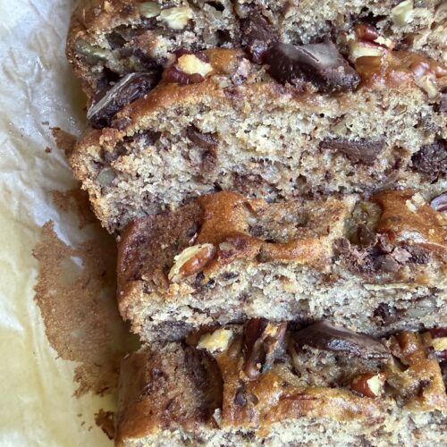 Banana nut bread with chocolate chips sliced on a wooden cutting board