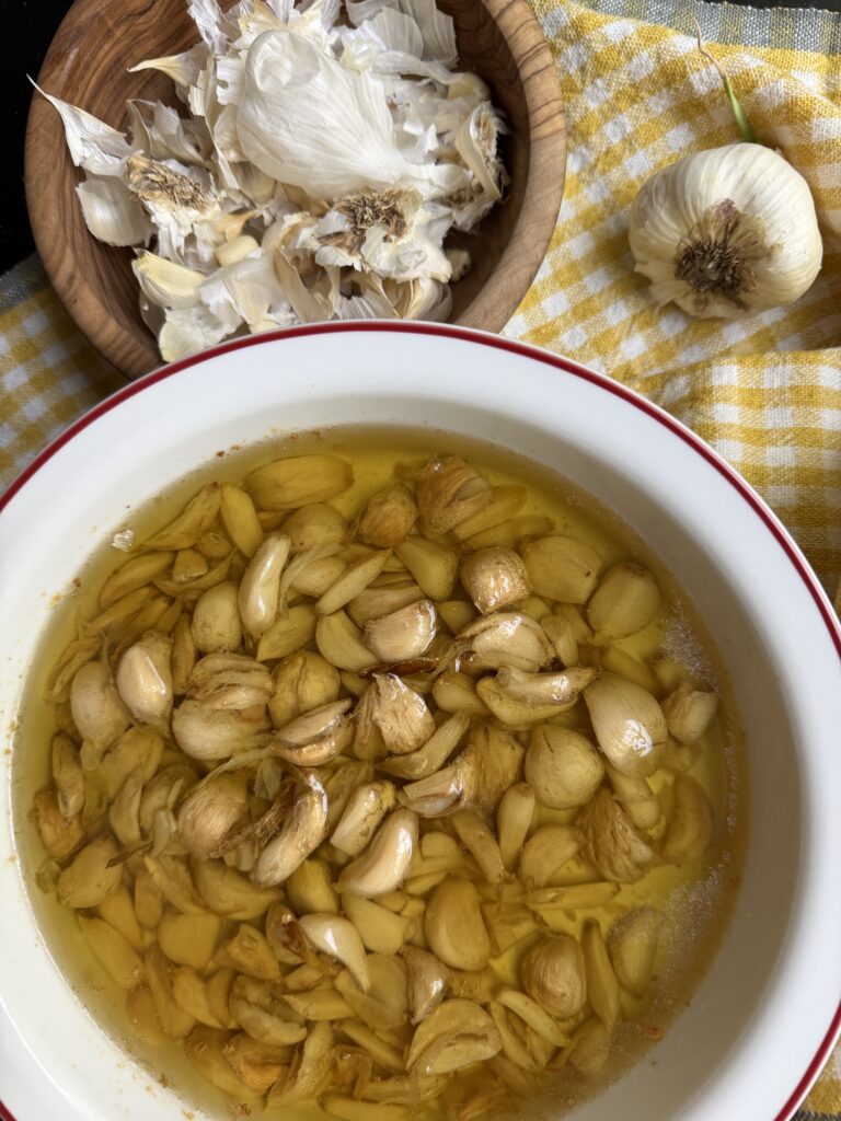 Garlic Confit finished product, in baking dish alongside garlic peels.