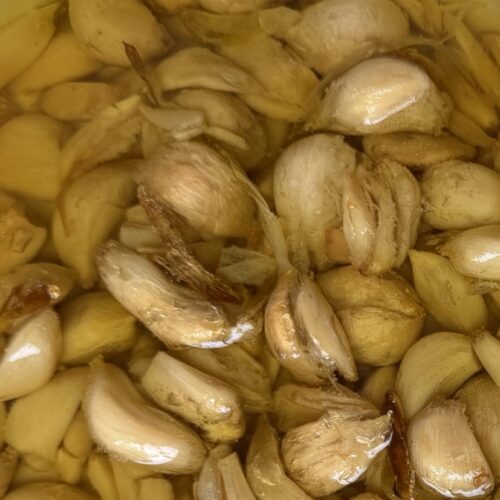 Garlic Confit finished product, in baking dish alongside garlic peels.