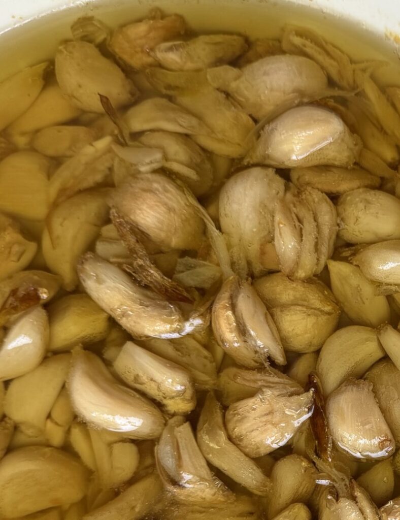 Garlic Confit finished product, in baking dish alongside garlic peels.