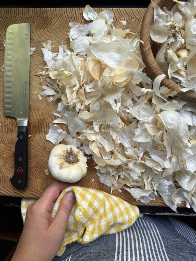Garlic skins and head of garlic on a chopping block with a chef's knife