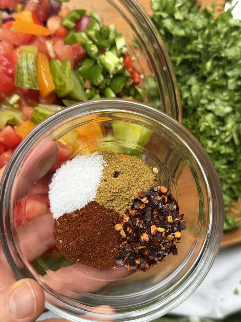 Diced vegetables in a bowl with cilantro on the side and spices in a smaller bowl.