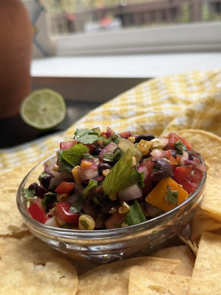 Black bean and corn salsa in a clear bowl with tortilla chips.